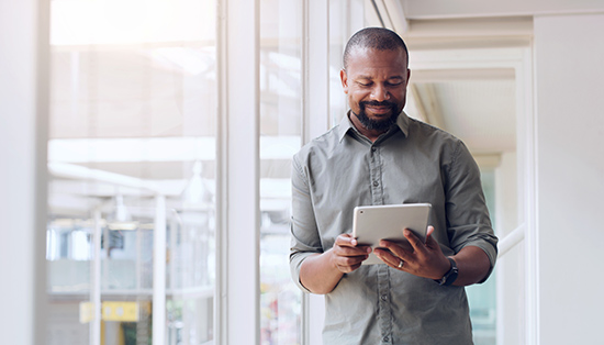 Man standing in an office looking at a tablet.